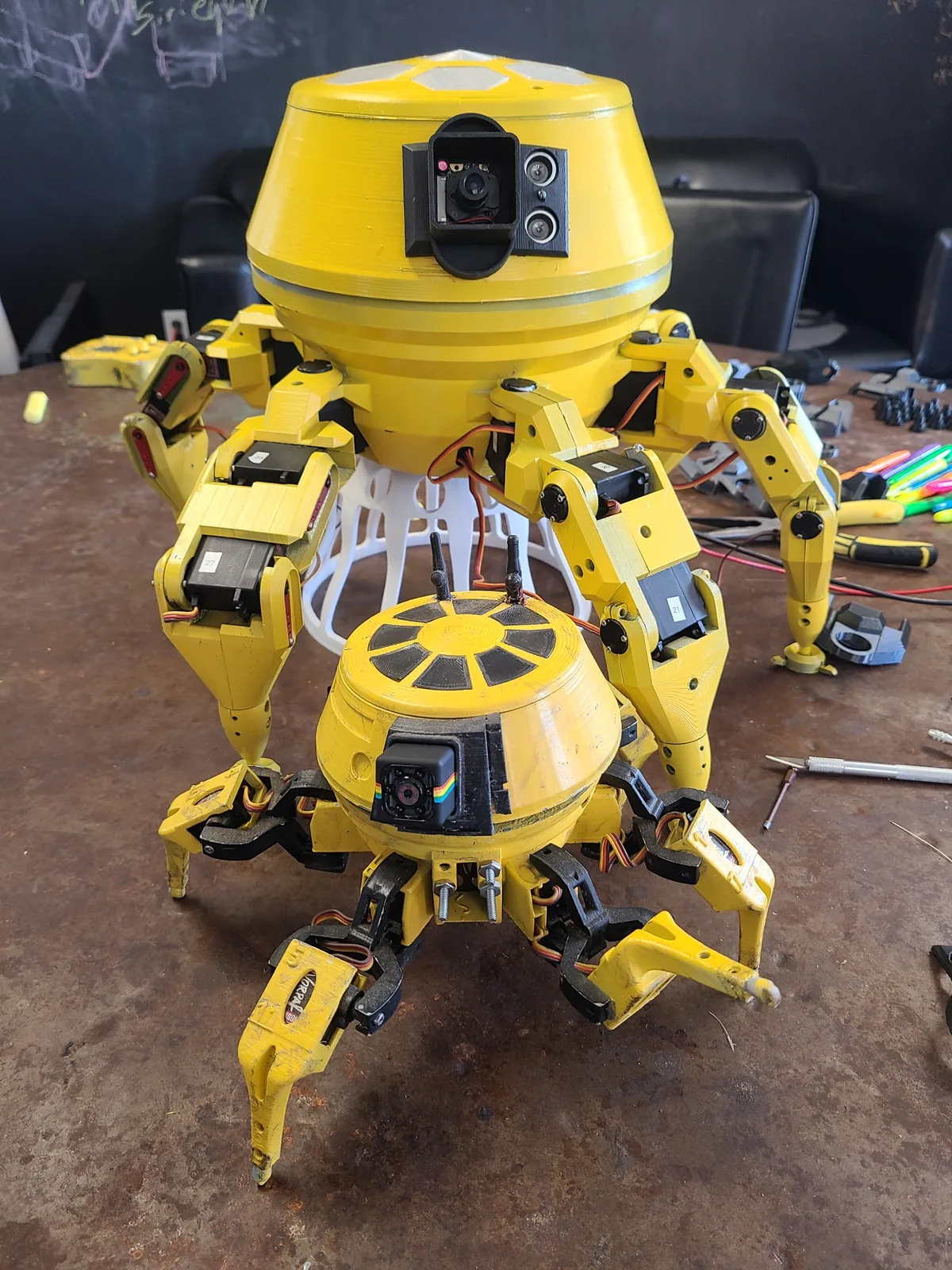 Small Skuttlebot prototype in front of a much larger yellow hexapod robot